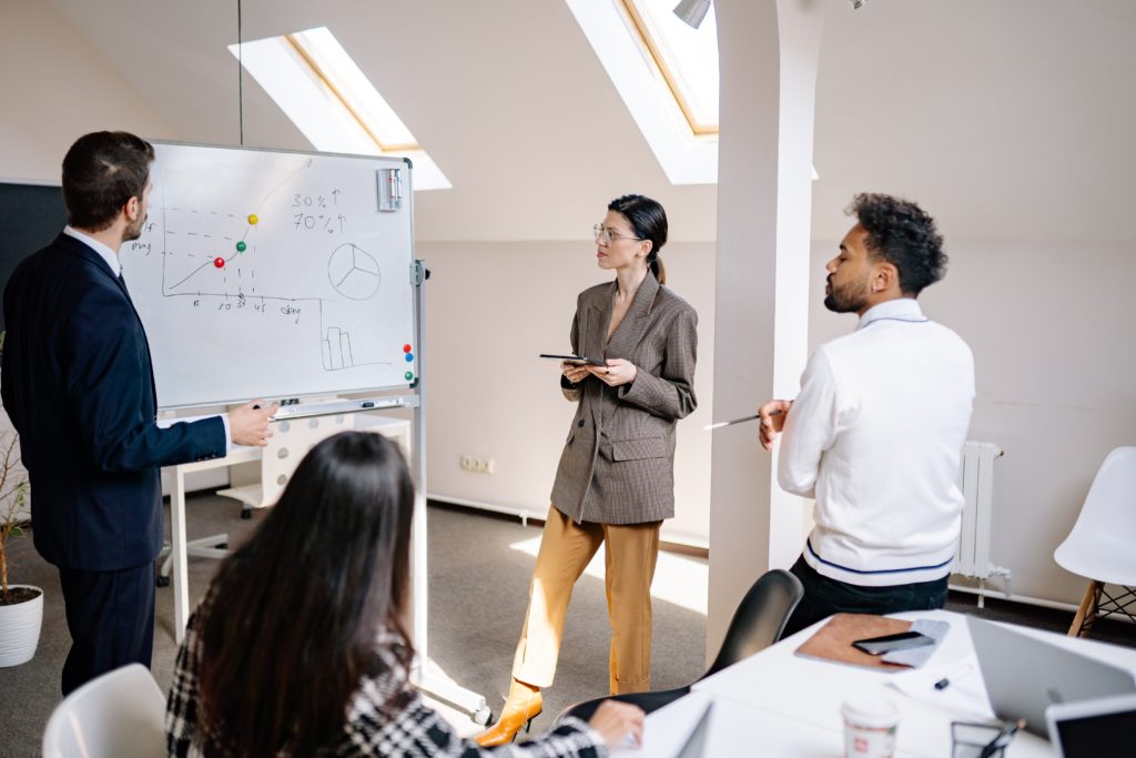 Group of four employees standing around a whiteboard that shows some charts.