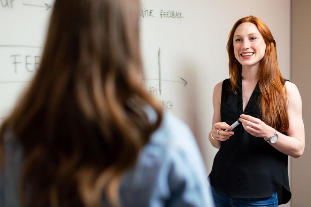 A smiling woman presenting her ideas while standing in front of a whiteboard