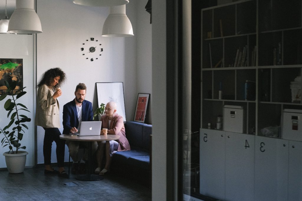 Three people gather around a laptop inside an office building.