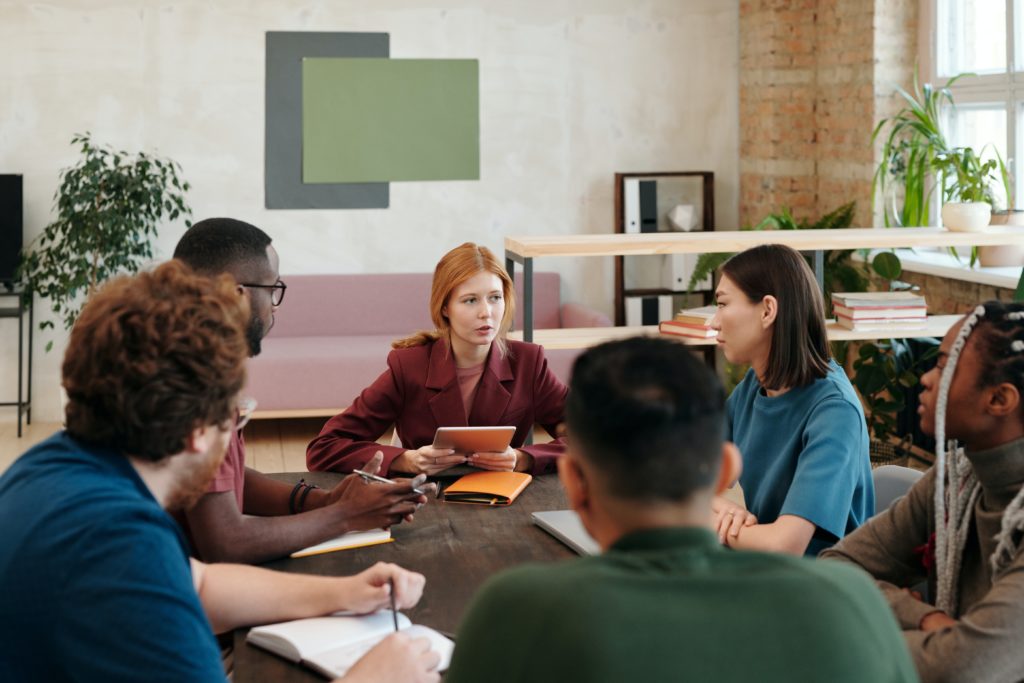 Six people having a discussion, while sitting around a table inside a modern office building.