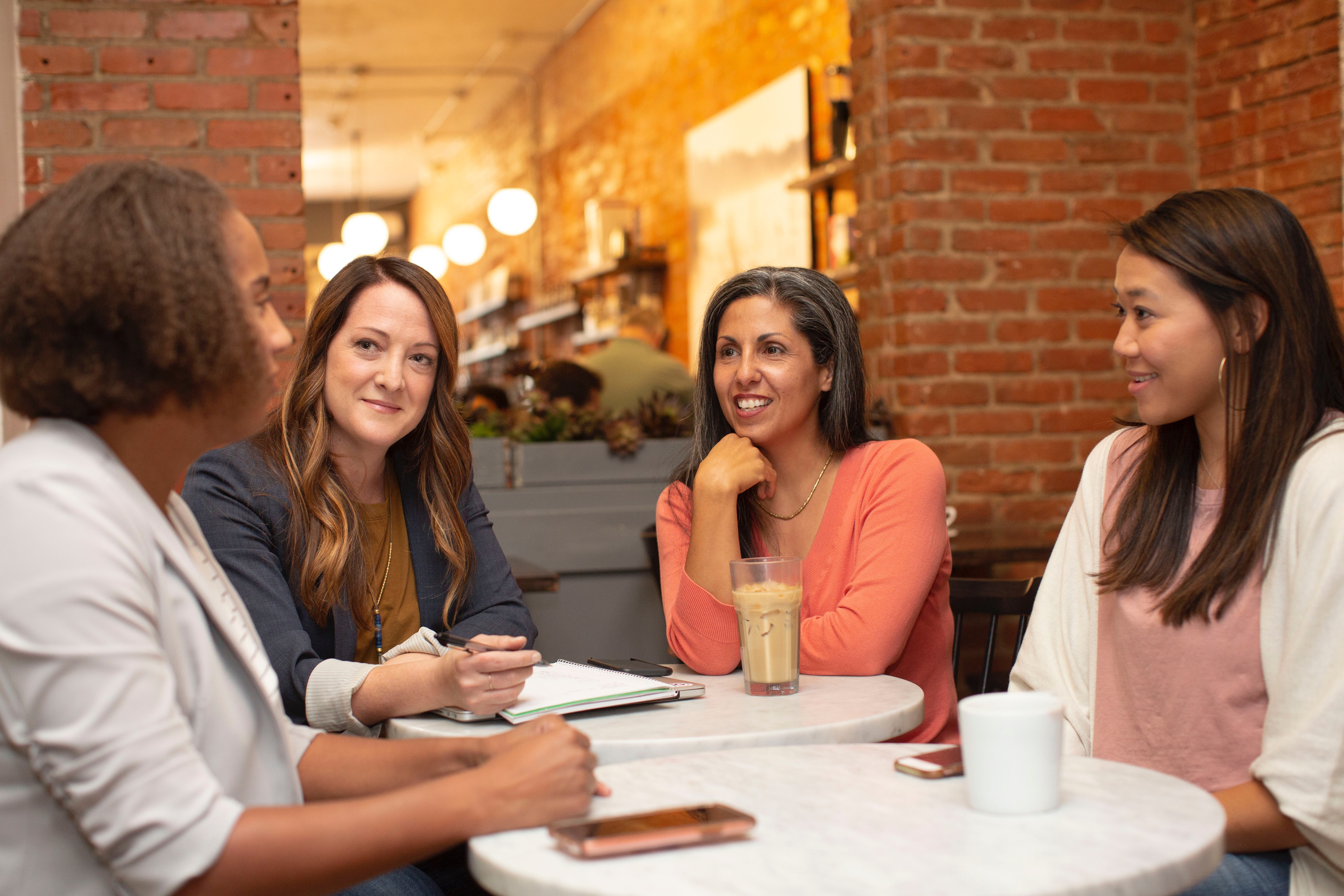 A group of four women sit together around a table, smiling.