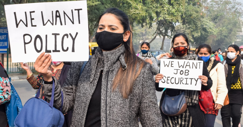 A woman holding up a sign saying ‘We Want Policy’ while marching in a street with others.