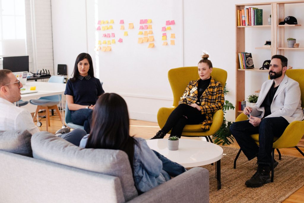 A team of five people meet around a small table in an office building.