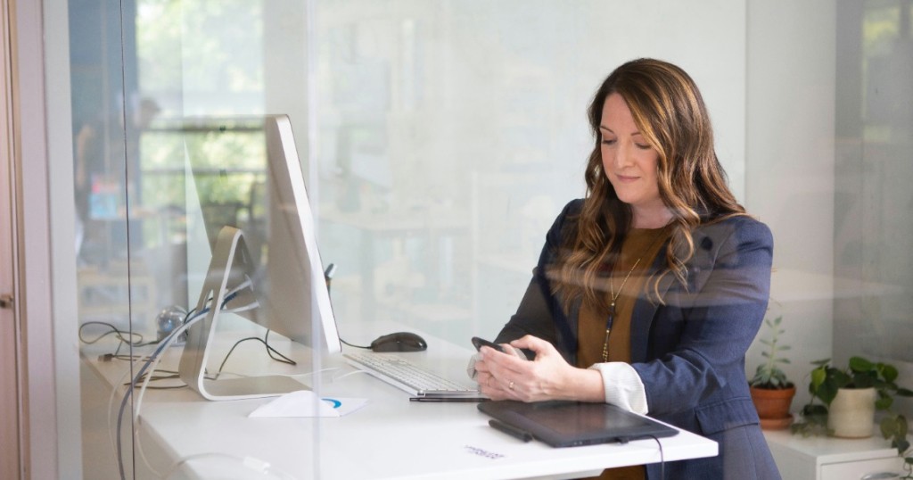 Woman sitting at a desk, looking down at her phone.